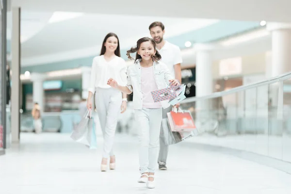 Família, pai, mãe e filha estão caminhando para outra loja no shopping center. A rapariga está a correr. . — Fotografia de Stock