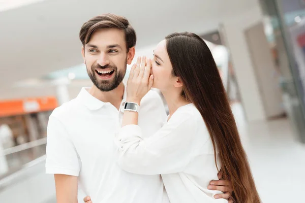 Man and woman in shopping mall. Girl is whispering in man's ear. — Stock Photo, Image
