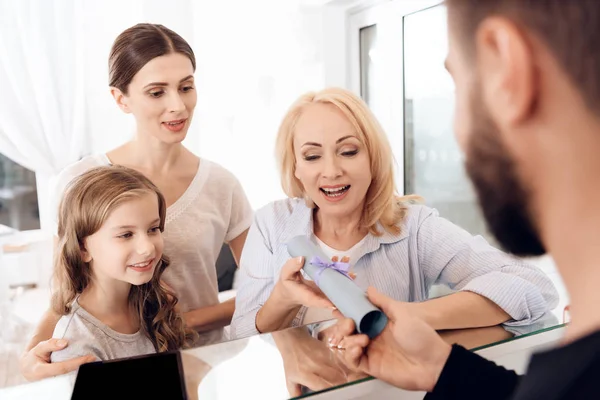 Happy mature woman with woman and little girl receives certificate for free visit to beauty salon.