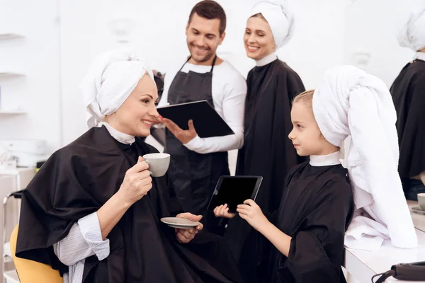 Niña con toalla en la cabeza muestra peinados en la tableta a la abuela, que bebe café . — Foto de Stock