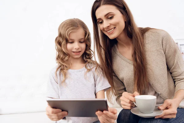 Krullend meisje met mooi bruin haar moeder Kies kapsel op Tablet PC. — Stockfoto