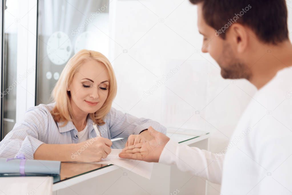 Mature beautiful woman fills out form for obtaining certificate to visit of beauty salon.