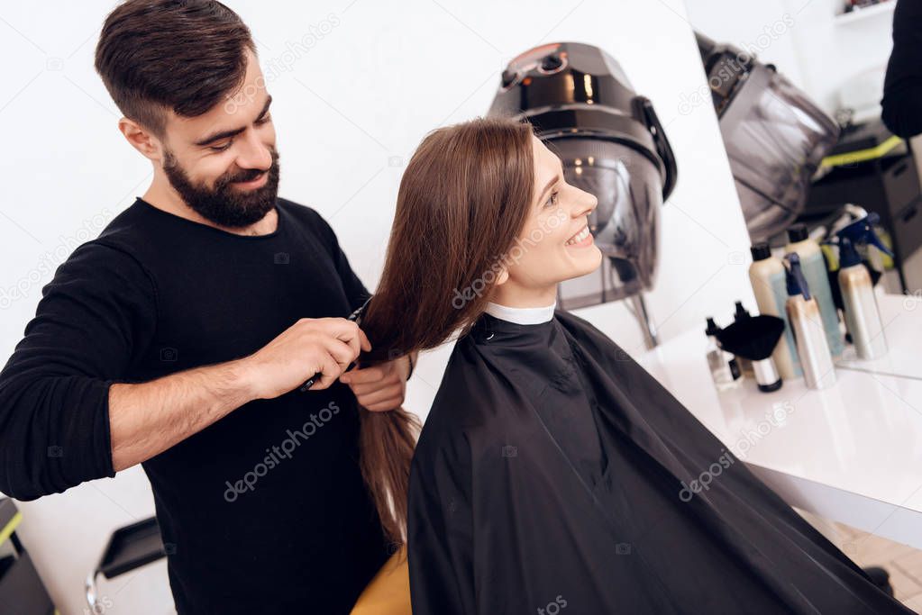 Hairdresser stylist is combing young woman with brown hair with hairbrush.