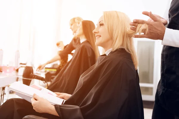 Female stylist combs blond straight hair of mature woman in beauty salon. — Stock Photo, Image