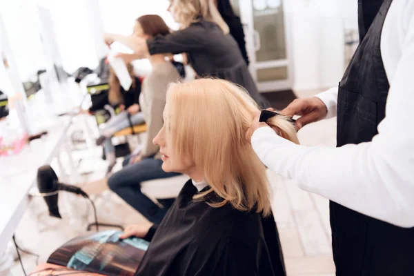 Estilista femenina peina cabello rubio y liso de mujer madura en salón de belleza . —  Fotos de Stock