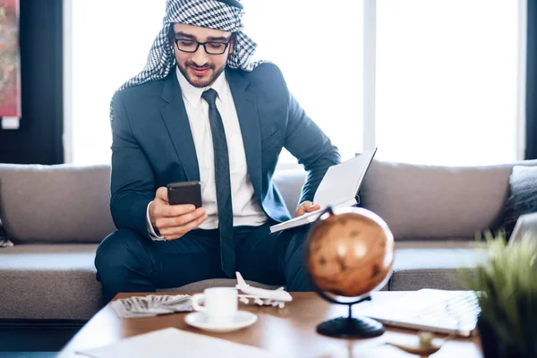 Arabisk affärsman på telefon med anteckningsbok på soffan på hotellrum. — Stockfoto