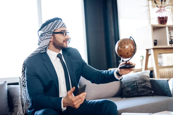 Арабский бизнесмен смотрит на глобус на диване в гостиничном номере . — стоковое фото