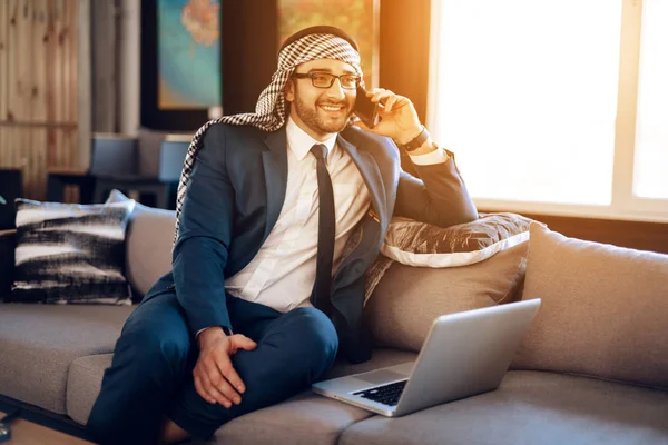 Arabischer Geschäftsmann telefoniert auf Couch im Hotelzimmer. — Stockfoto