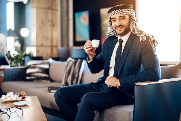 Arabisk affärsman dricka kaffe på soffan på hotellrum. — Stockfoto