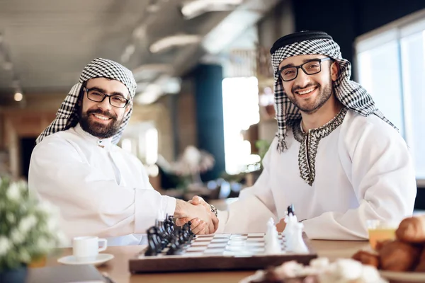 Twee Arabische zakenlieden schudden handen achter het schaakbord op hotelkamer. — Stockfoto