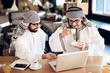 Two arab businessmen drinking coffee at table at hotel room.