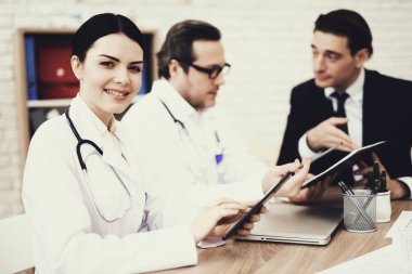 Tablet tıbbi ofis içinde yazarak tatmin hemşire. Bulanık doktor ve hasta arka planda.