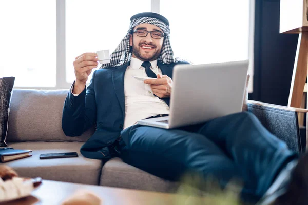 Entspannter arabischer Geschäftsmann auf Lapton mit Kaffee auf der Couch im Hotelzimmer. — Stockfoto