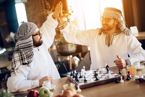 Two arab businessmen high five behind chessboard at hotel room. — Stockfoto