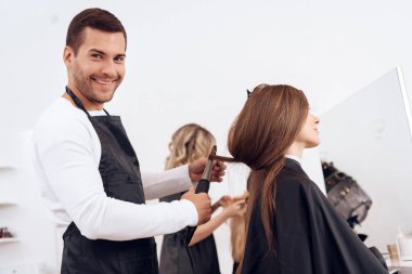 Hairdresser curling brown hair of beautiful woman. Woman care about hairstyle.