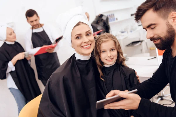 Gelukkig jonge vrouw met handdoek op hoofd en krullend meisje raadplegen met stylist. — Stockfoto