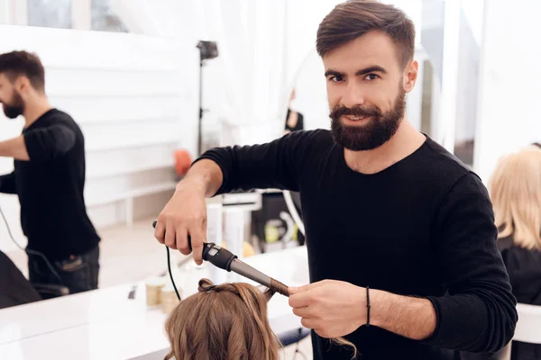 Barbero barbudo hace rizos en el pelo de hermosa niña con rizador de pelo . —  Fotos de Stock