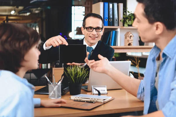 Realtor zittend op Bureau in kantoor. Man toont Tablet aan vader en zoon. — Stockfoto