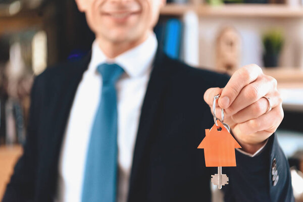 Риэлтор сидит за столом в офисе. Риэлтор показывает ключи с вырезанным значком нового дома
.