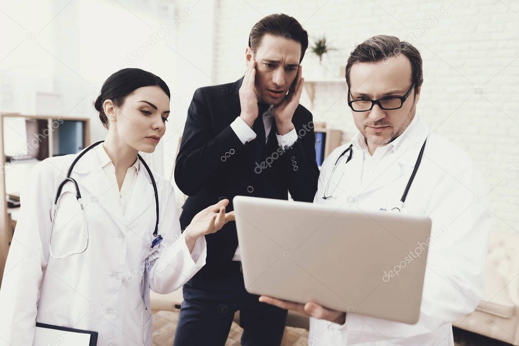 Anxious businessman looks at laptop screen in hands of doctor. Medical examination.