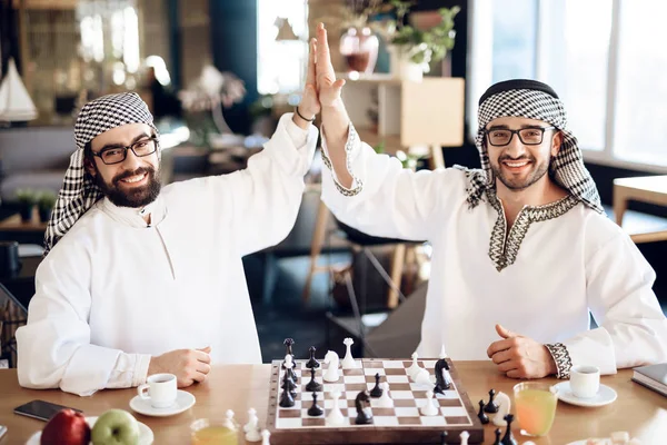 Two arab businessmen high five behind chessboard at hotel room. — Stockfoto