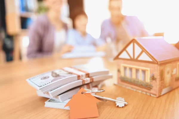 Cerca de llaves, dinero y casa modelo con la familia en el fondo . — Foto de Stock