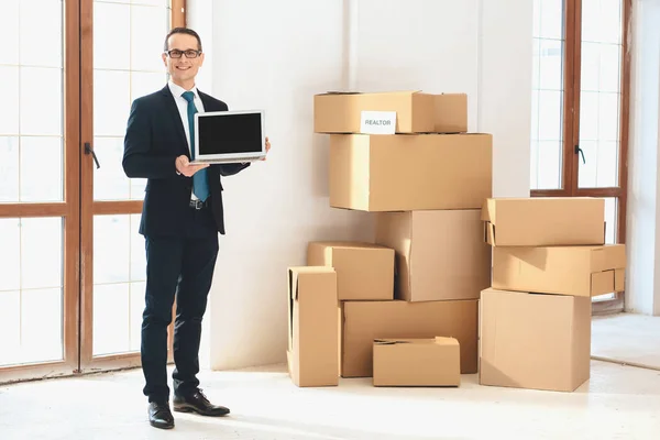 Realtor presenting laptop in new apartment with cardboard boxes.