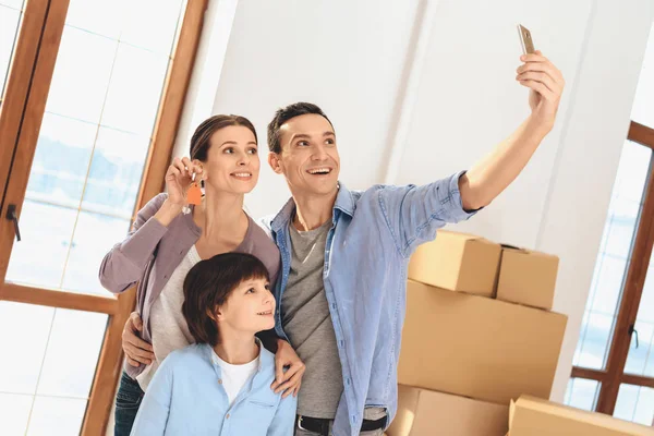 Ayah, ibu dan anak di apartemen baru dengan kotak kardus. Keluarga mengambil selfie . — Stok Foto