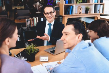 Emlak ofis masasında oturuyor. Emlakçı tablet baba, anne ve oğlu için gösterilen.