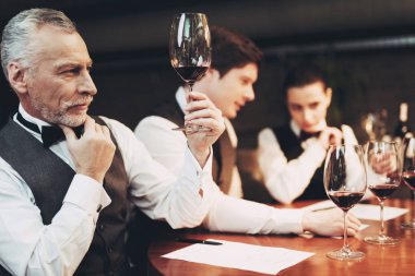 Papyon eski deneyimli sommelier masada otururken bir bardak kırmızı şarap tutuyor.