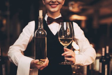 Yakın çekim. Bir şişe kırmızı şarap ve bardak, holding neşeli zarif garson ayakta yakınındaki bar.