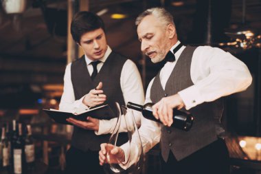 Two experienced sommeliers taste wine. Sommelier pours red wine from bottle into decanter. Wine tasting. Male skilled sommelier estimates alcoholic drink.