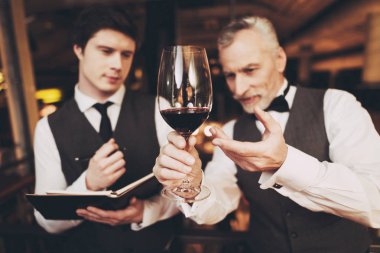 Two experienced sommeliers taste red wine and make wine list in restaurant.