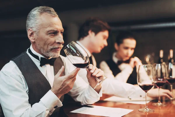 Old experienced sommelier in bow tie is tasting wine in glass. Wine tasting. — Stock Photo, Image