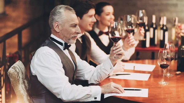 Three sommeliers assess taste and color qualities of wine when examining glass in restaurant. — Stock Photo, Image