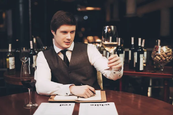 Αυτοπεποίθηση sommelier κάνει κρασί κάρτα σε εστιατόριο, καθιστώντας σημειώσεις και βλέποντας το ποτήρι λευκό κρασί. — Φωτογραφία Αρχείου