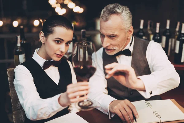 Old experienced sommelier tells young girl about specifics of taste of red wine in restaurant. — Stock Photo, Image