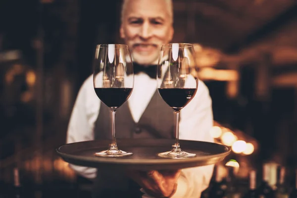蓬松的侍酒师与领结举行托盘与一杯葡萄酒。服务员拿着托盘与饮料. — 图库照片