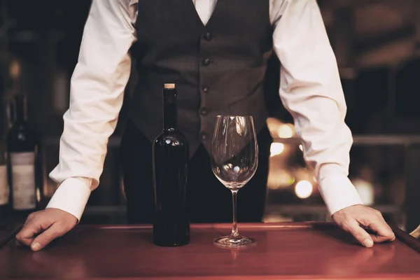 Waiter stands before tray with bottle of wine and empty glass in restaurant. Wine tasting concept. — Stock Photo, Image