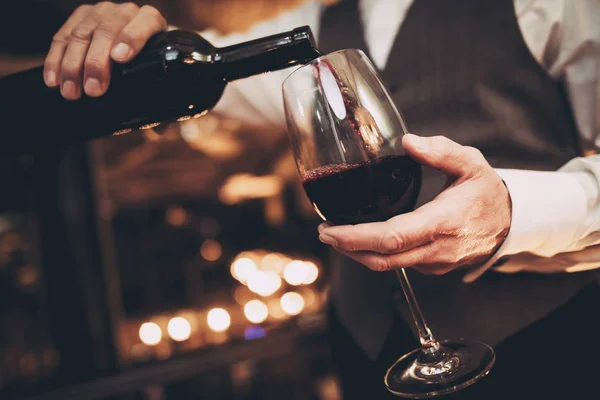 Close up. Elegant waiter pours red wine from bottle into glass at restaurant. — Stock Photo, Image