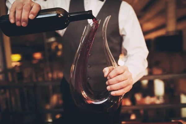 Fecha. Garçom elegante derrama vinho tinto de garrafa em decantador no restaurante . — Fotografia de Stock
