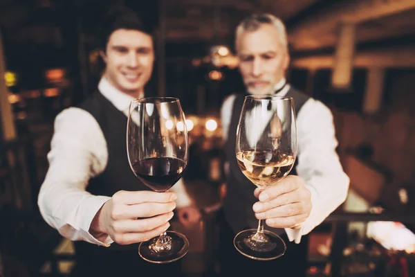 Sommeliers jóvenes y viejos están sosteniendo copas de vino tinto y blanco en el restaurante . — Foto de Stock