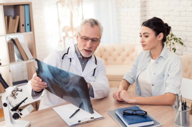 Doctor with stethoscope and female patient in office. Doctor is showing x-ray.