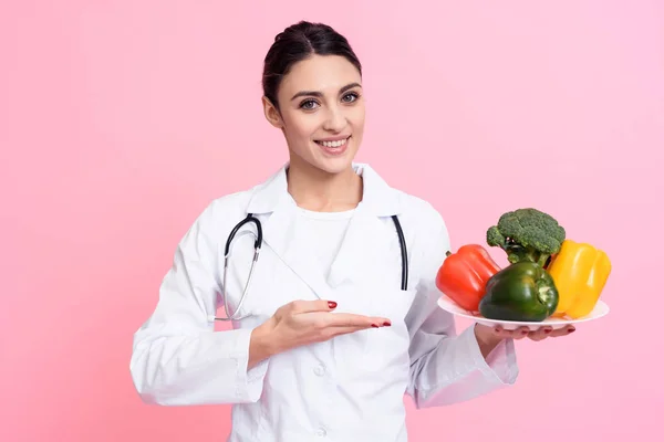 Портрет усміхненої жінки-лікаря зі стетоскопом, що тримає тарілку з овочами ізольовано . — стокове фото