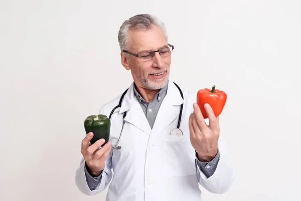 Portrait of doctor with stethoscope holding red and green peppers isolated. — Stock Photo, Image
