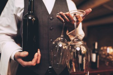 Close up. Sommelier in bow tie is holding with bottle of wine and wine glass. Blurred.
