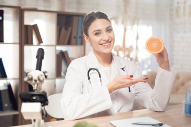 Kadın doktor stetoskop ile mikroskop ofis masasında oturuyor. Kadın turuncu tutuyor.