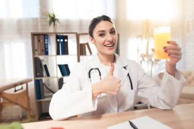 Kadın doktor stetoskop ile mikroskop ofis masasında oturuyor. Kadın suyu tutuyor.