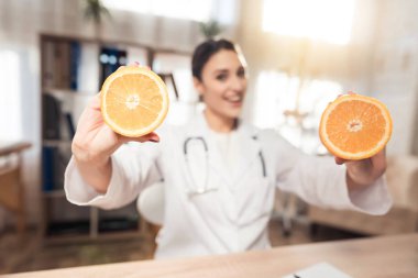 Kadın doktor stetoskop ile mikroskop ofis masasında oturuyor. Kadın portakal tutuyor.