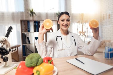 Kadın doktor stetoskop ile mikroskop ofis masasında oturuyor. Kadın portakal tutuyor.